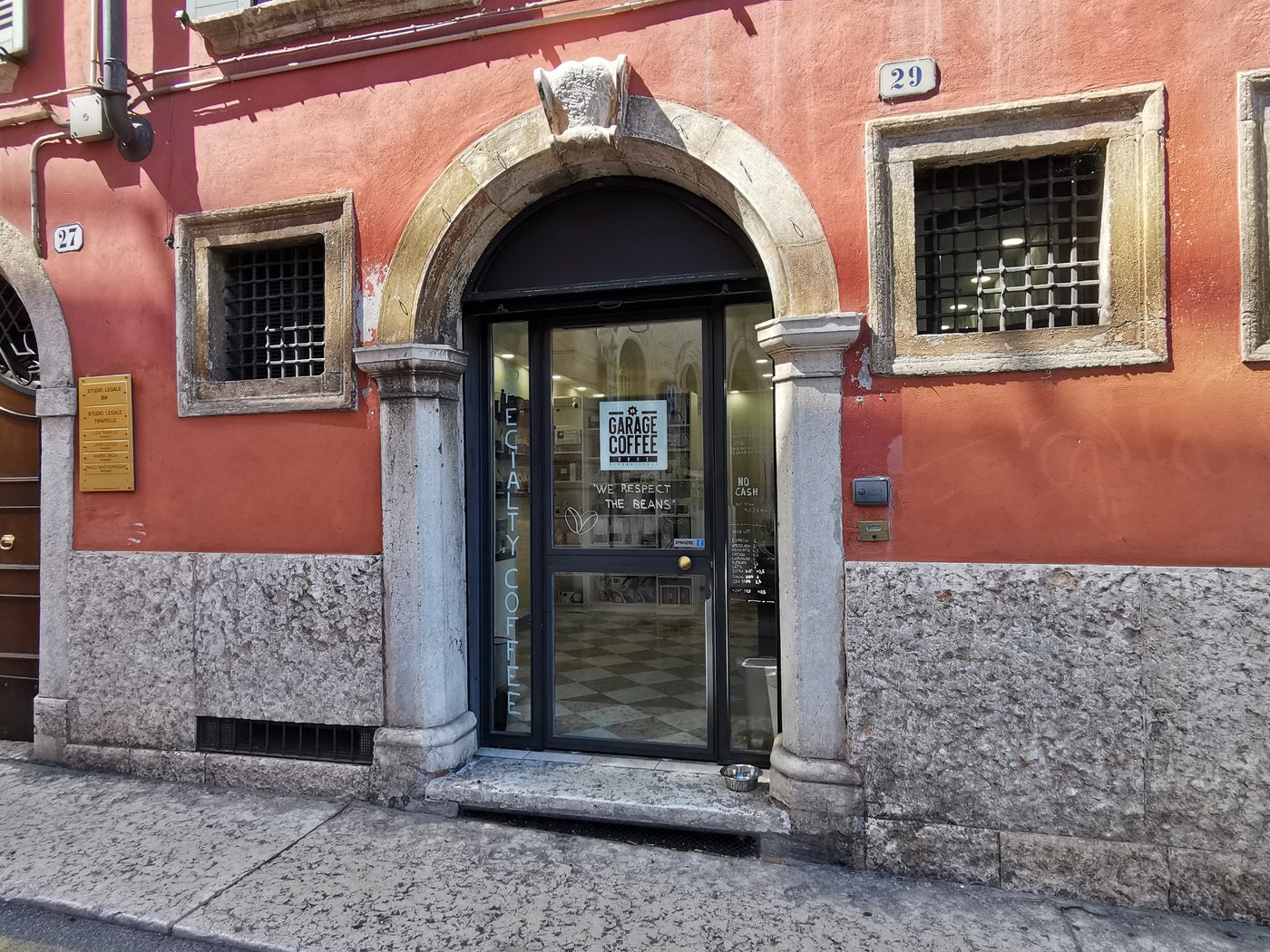 A stone archway storefront with Garage Coffee signage and Specialty Coffee lettering on the glass door, a dog bowl on the step