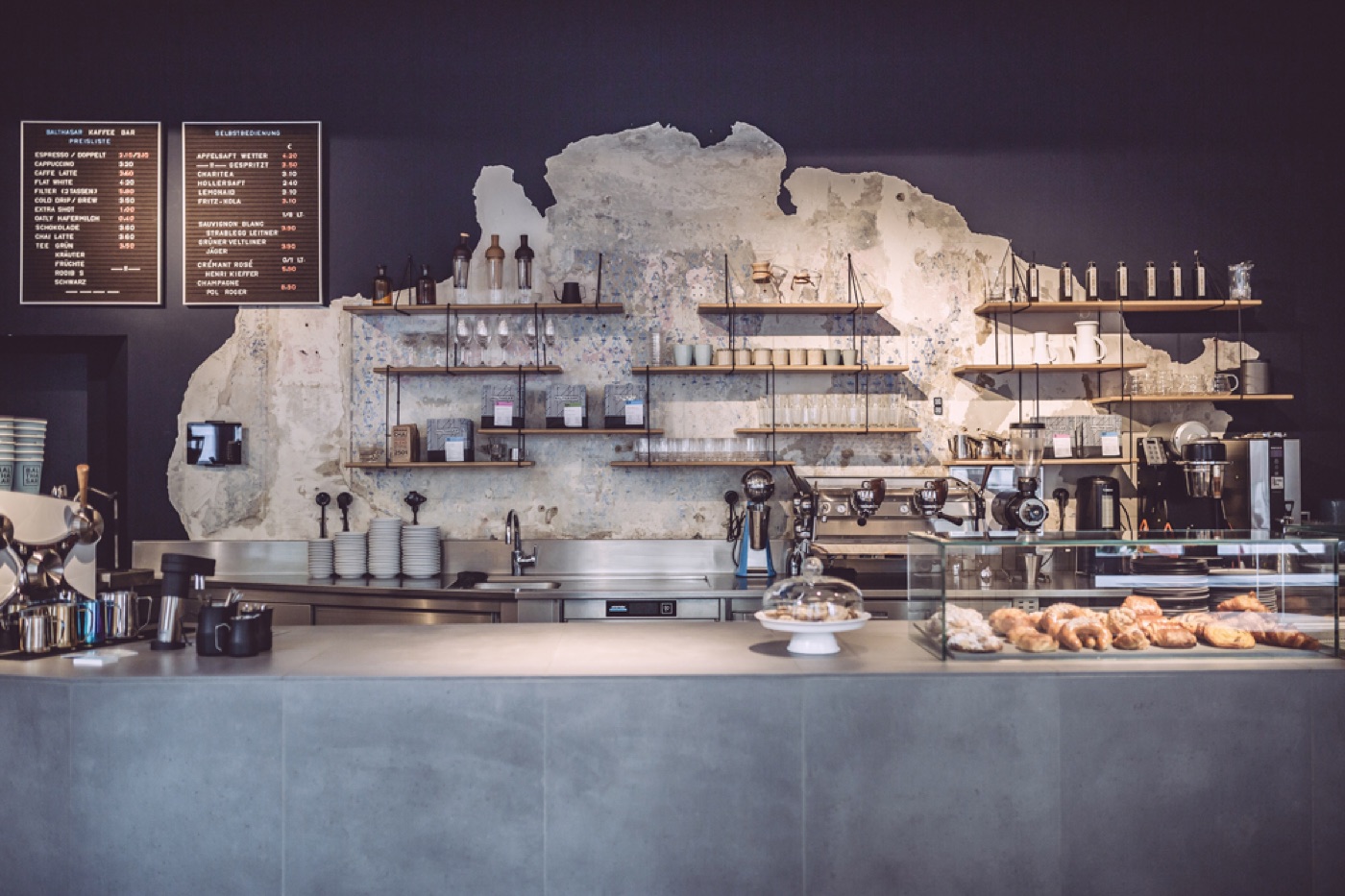 The mosaic-tiled counter at Balthasar Kaffee Bar, retail shelves and espresso machine against a weathered plaster wall