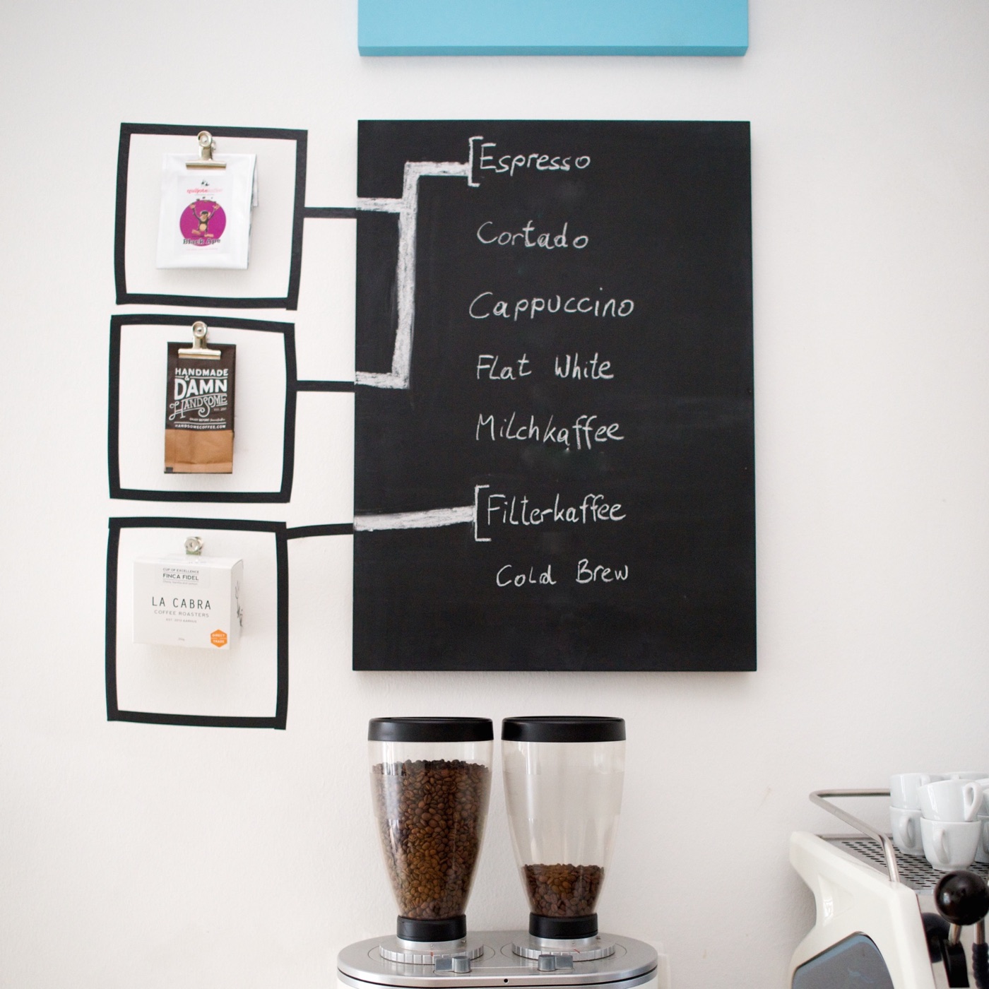 Retail coffee bags clipped to the wall beside a hand-chalked drinks menu at Kaffeemodul, grinders below