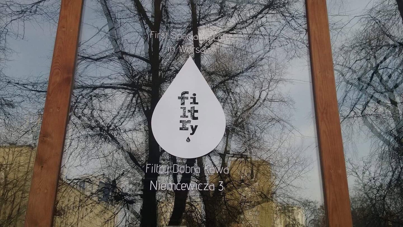 A water drop shaped window decal reading Filtry, First Specialty Cafe in Warsaw, on the shop's front window