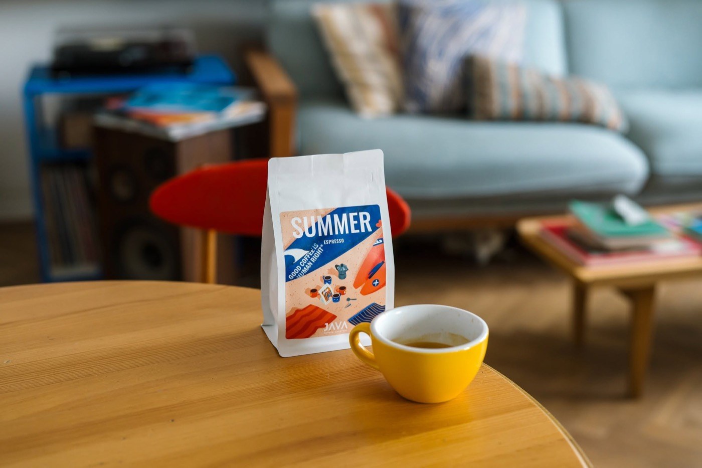 A retail bag of JAVA's Summer espresso blend beside a yellow espresso cup on a wooden table