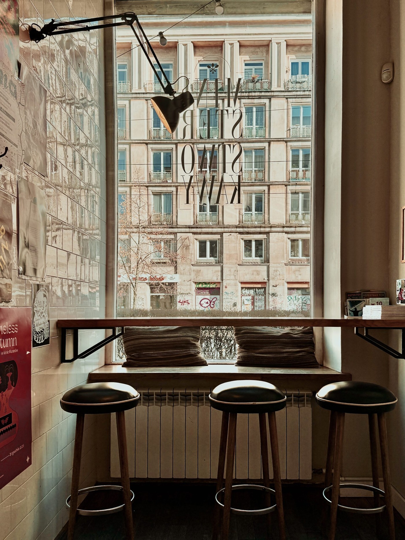A window seat with striped cushions and bar stools beneath the Ministerstwo Kawy lettering etched into the glass
