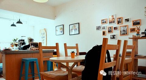 The compact interior with wooden chairs and tables, a service counter with blue stools, and framed pictures on a white wall
