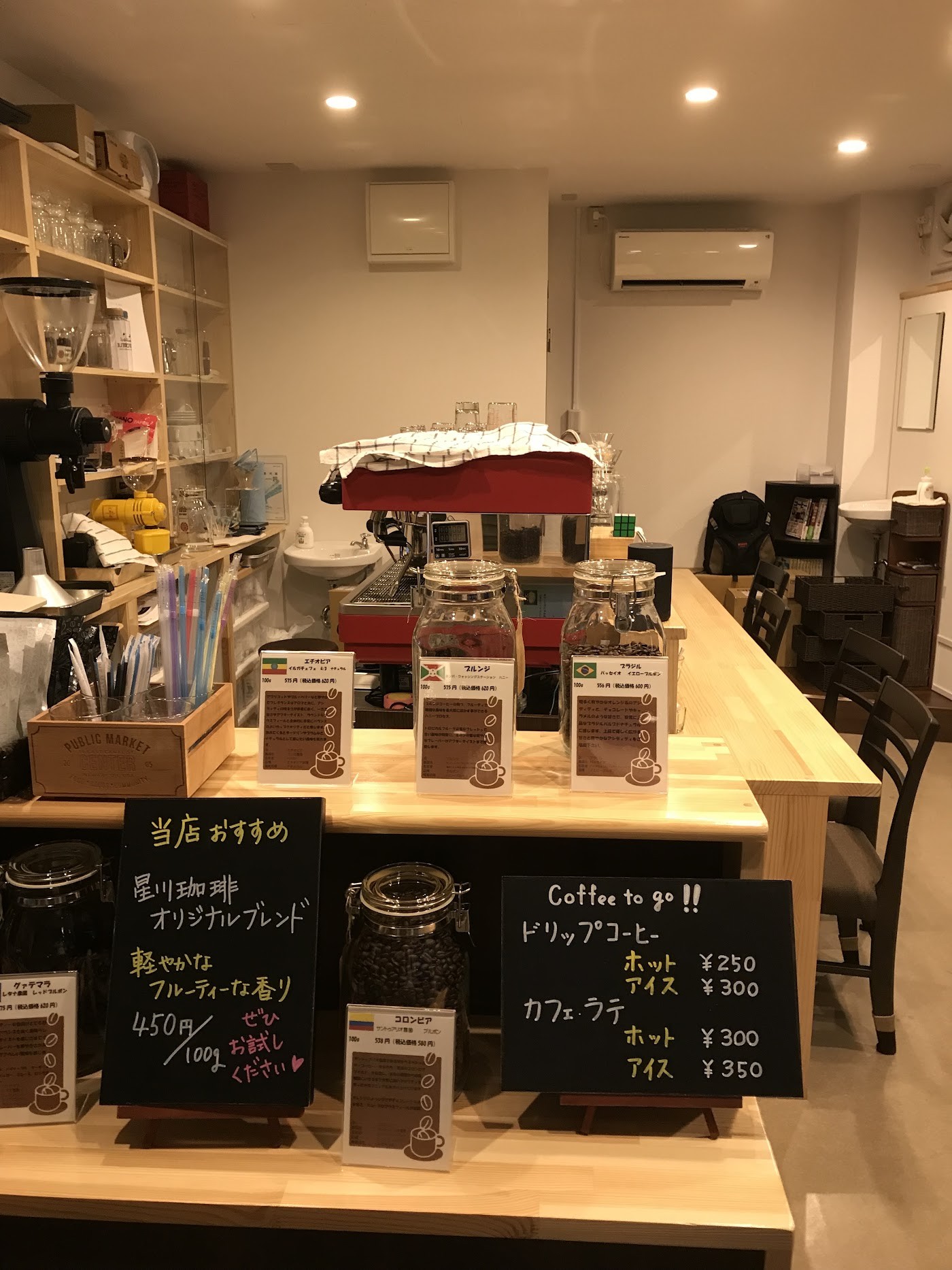 The wooden counter inside Hoshikawa Coffee with a red espresso machine, glass jars of beans, hand written chalkboard price signs and shelves of brewing gear