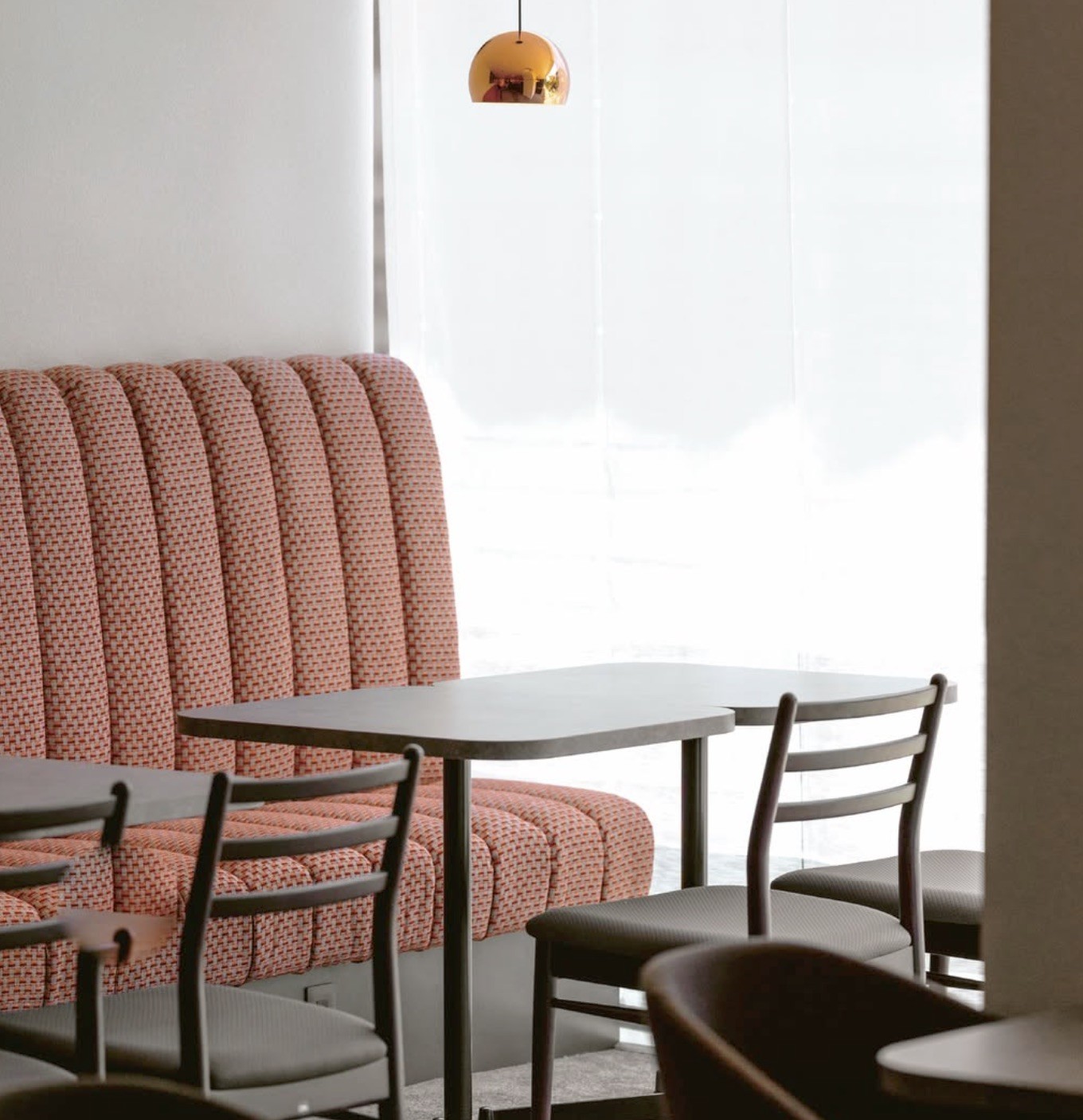 The seating area with a pink patterned booth, dark wood tables, and a copper globe pendant light by the window