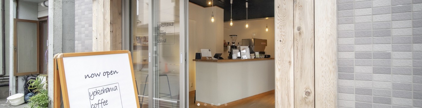 The open storefront with a now open sandwich board out front, and a wood counter with an espresso machine and hanging pendant lights inside