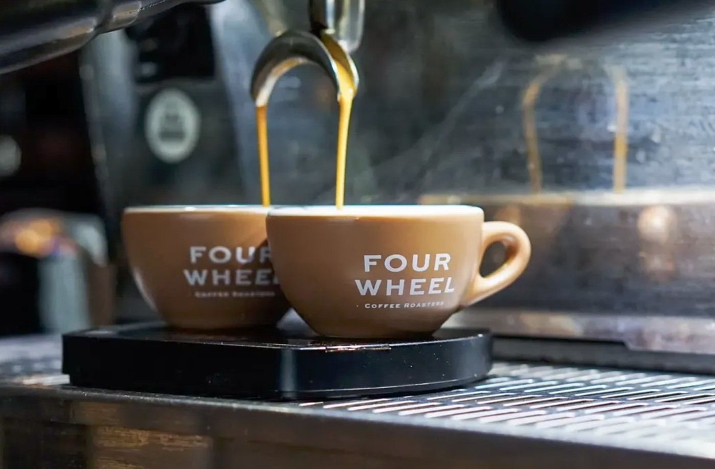 Espresso pouring into two branded FOUR WHEEL Coffee Roasters cups on the group head scale