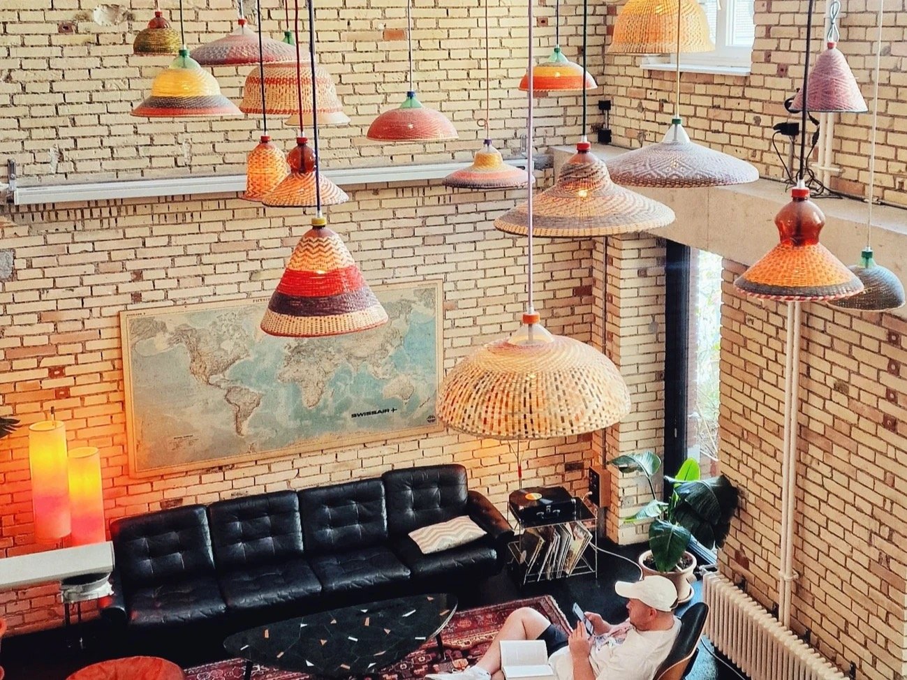 The lounge area at Auer & Co., woven pendant lampshades hanging over a leather sofa and exposed brick wall