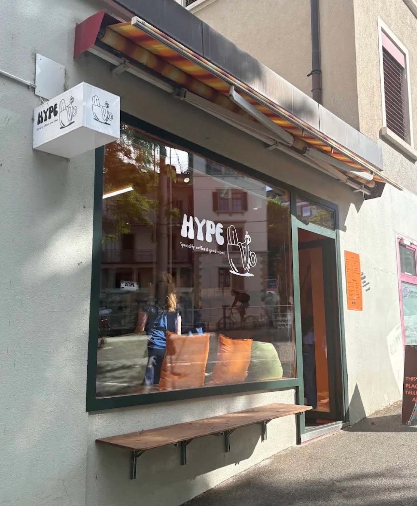 The Hype storefront window with its hand drawn logo, striped awning, and a bench out front
